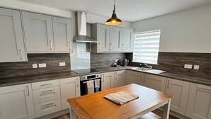 Una cocina moderna con armarios grises claros, una mesa de madera y una lámpara colgante.