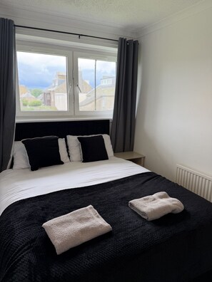 Ein ordentlich bezogenes Bett mit einem schwarz-weißen Duvet, zwei Handtüchern und einem fenster mit Vorhängen.