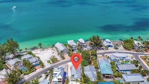 Vue aérienne d’une zone résidentielle côtière, avec des maisons, une plage et des eaux turquoise limpides.