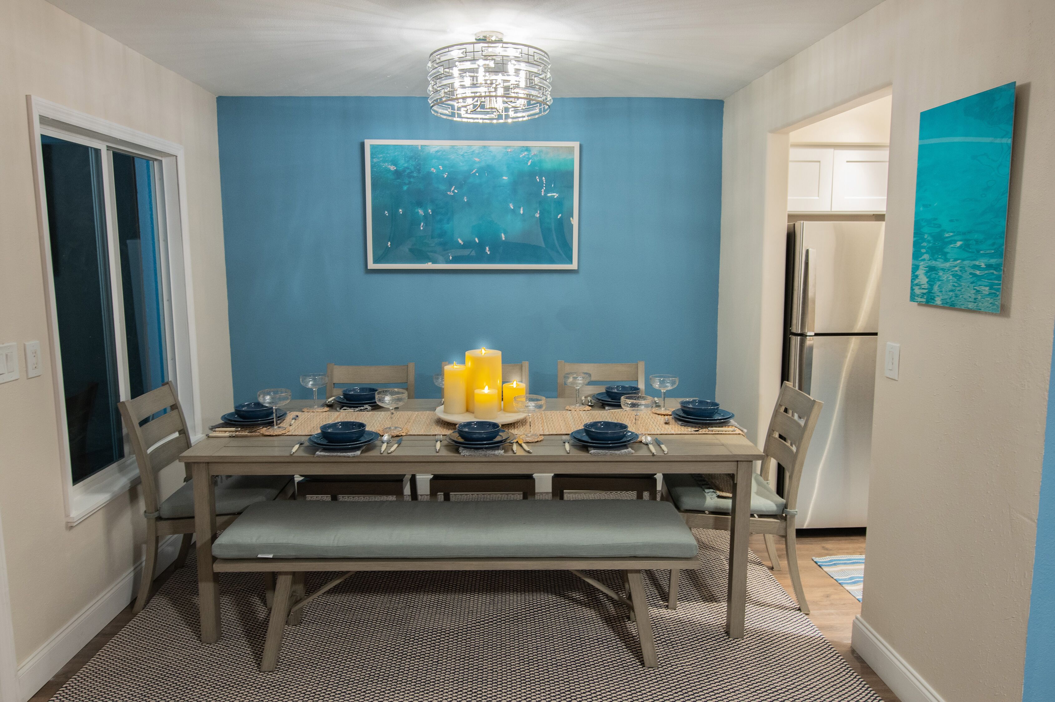 Une salle à manger avec un mur d’accent bleu, un lustre et un grand tableau.