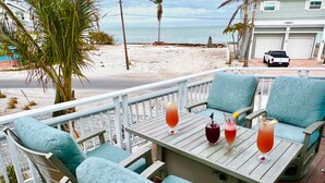 Une terrasse avec une table et des chaises, donnant sur une plage et l’océan.