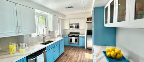 A modern kitchen with blue cabinets, stainless steel appliances, and a wooden floor.