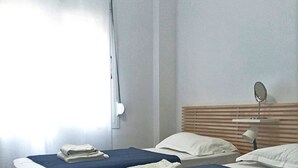 A hotel room with two beds, a wooden headboard, a bedside table with a lamp, and a window with blinds. - Apart in the Heart Of Athens (Athina)