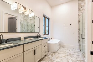 A modern bathroom with a large mirror, dual sinks, a freestanding bathtub, and a glass-enclosed shower.