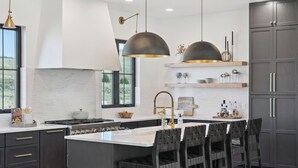 Una cucina moderna con mobili scuri, un'isola centrale con sgabelli da bar, illuminazione a sospensione e vista sull'esterno.