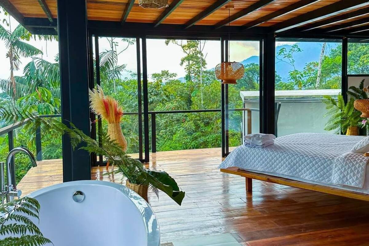 A modern room with a large bathtub, a bed, and a view of lush greenery.