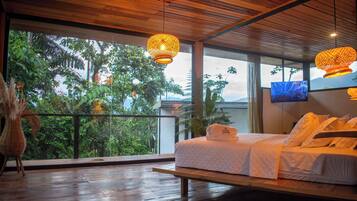 Un dormitorio con cama, suelo de madera, ventana grande y lámparas colgantes.