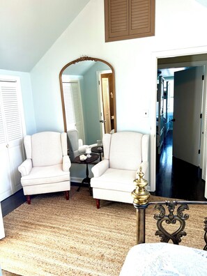 A room with two white armchairs, a large mirror, a small table with a candle, and a bed with a headboard. - Bernie Beach House And Bungalow  (Lavallette)