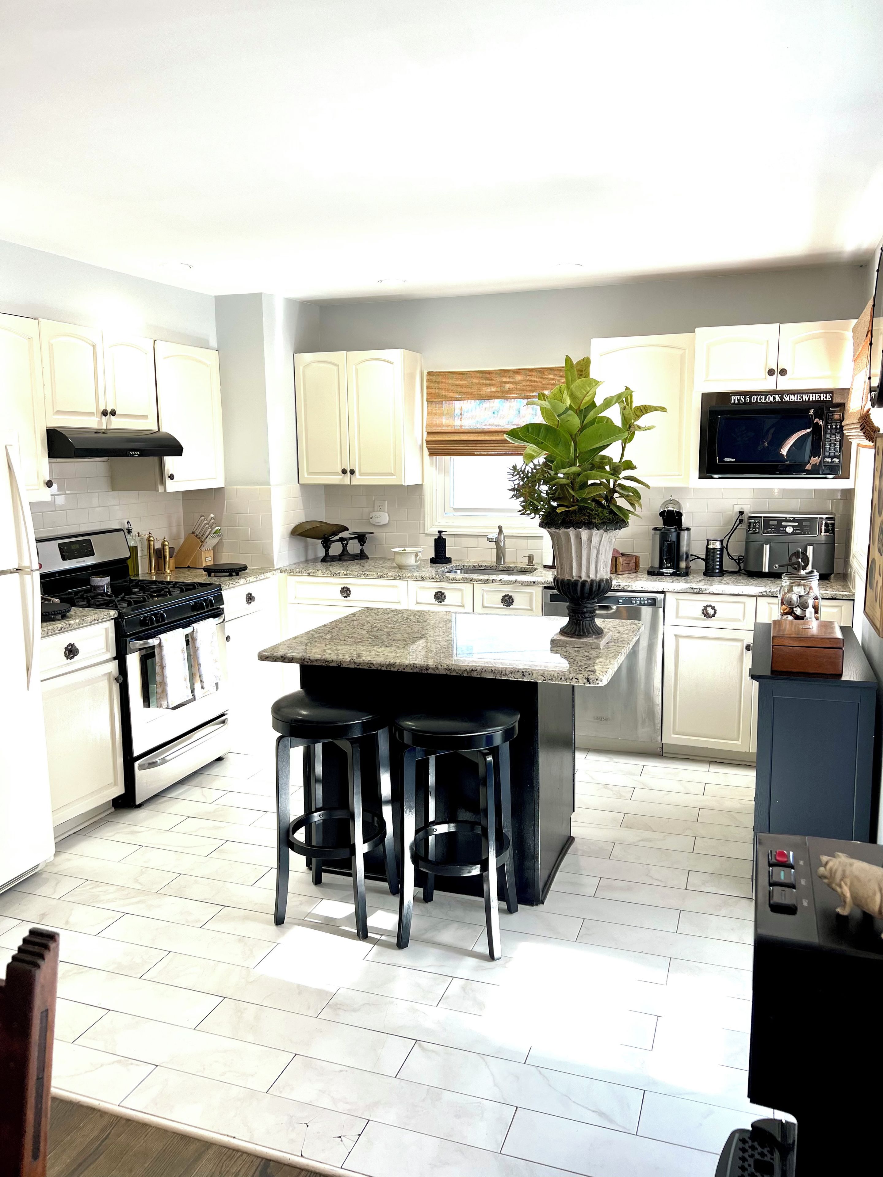 A modern kitchen with white cabinetry, a central island with stools, a built-in oven, and a microwave above the island.