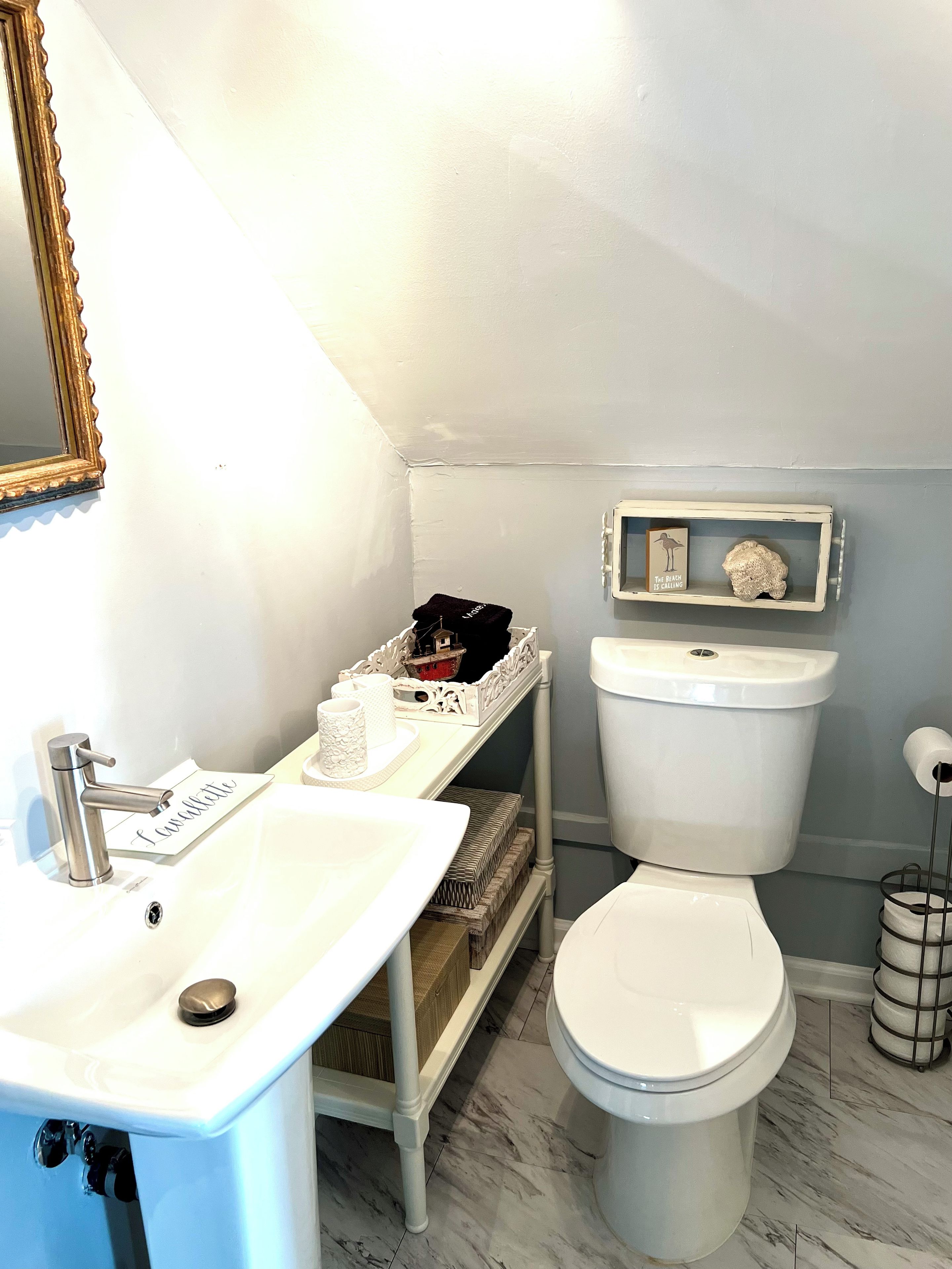 Une salle de bain avec un lavabo blanc, des toilettes et une étagère ornée d’objets décoratifs.