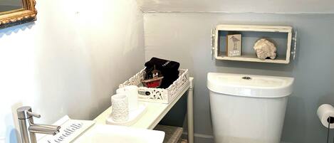 Une salle de bain avec un lavabo blanc, des toilettes et une étagère ornée d’objets décoratifs.