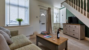 Ein Wohnzimmer mit einer Couch, einem Couchtisch mit Büchern und einer Flasche, einem Fernseher auf einem Schrank und einer Treppe.