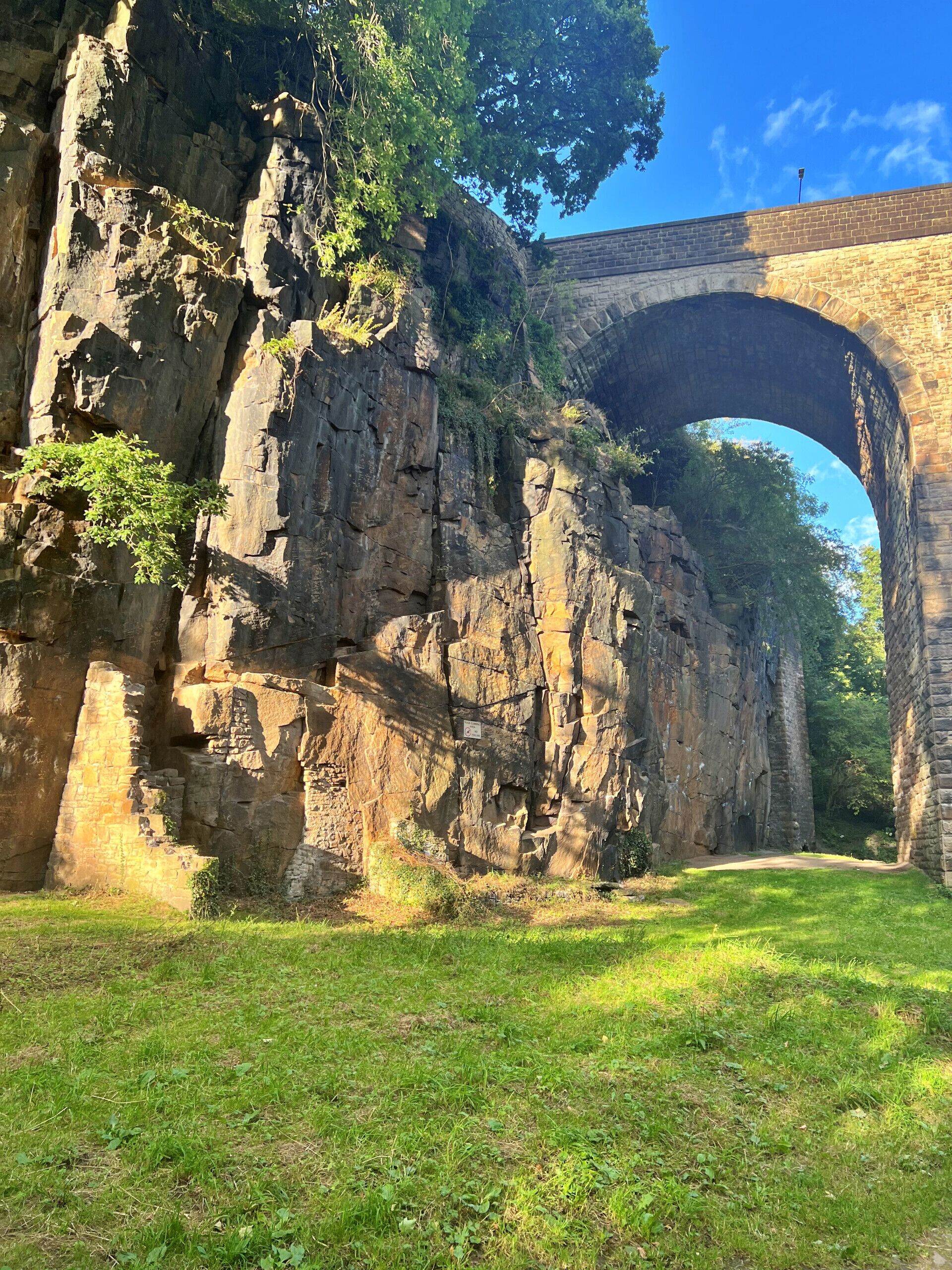A stone bridge arching over a rocky cliff with grass in the foreground.