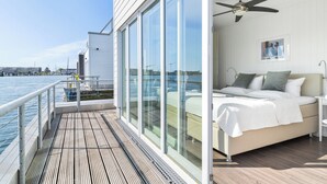 A bedroom with a bed, a ceiling fan, and a large window overlooking the water.