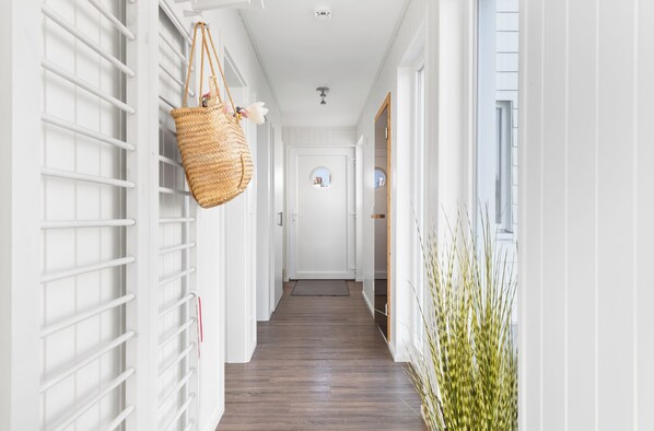 A hallway with a white door at the end, a hanging basket, and a plant on the right. - Triton: Meerblick, Sauna, Dachterrasse (Olpenitz)