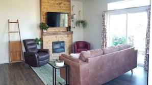 Ein Wohnzimmer mit Kamin, einer Couch, einem Sessel, einem kleinen Tisch und einer Leiter.