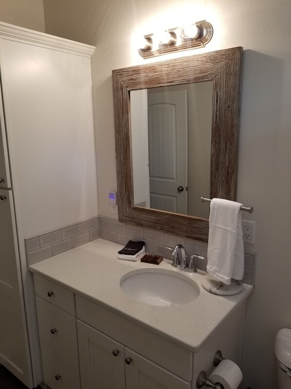 A bathroom with a white vanity, a mirror with a wooden frame, a towel rack, and a toilet paper holder.
