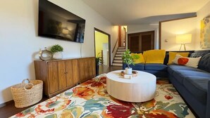 A living room with a round coffee table, a blue sofa, a wooden cabinet, and a TV mounted on the wall. - Spacious 5BR Olympia retreat with private yard, pond, near Capitol and trails (Olympia)