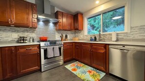 A modern kitchen with wooden cabinets, a stainless steel stove, and a dishwasher. - Spacious 5BR Olympia retreat with private yard, pond, near Capitol and trails (Olympia)