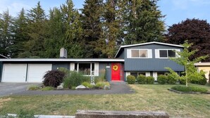 A two-story house with a red door, garage, and a well-maintained lawn. - Spacious 5BR Olympia retreat with private yard, pond, near Capitol and trails (Olympia)