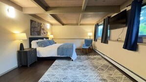 A bedroom with a bed, bedside tables, a chair, a rug, and a TV. - Spacious 5BR Olympia retreat with private yard, pond, near Capitol and trails (Olympia)