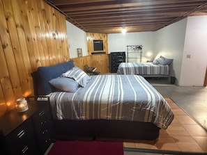 A bedroom with two beds, wooden walls, a dresser, and a nightstand.