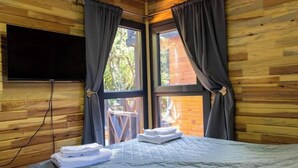 A room with a bed, a flat-screen TV mounted on the wall, and large windows with curtains. - Lion's Forest #4 (Burgas)