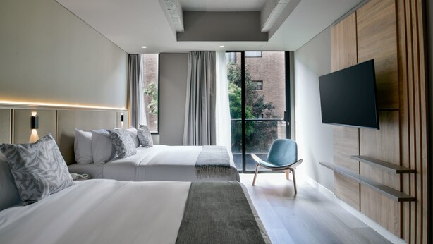 Ein modernes Hotelzimmer mit zwei Betten, einem Flachbildfernseher, einem Balkon mit Blick auf die Stadt und einer Wand mit Holzverkleidung.