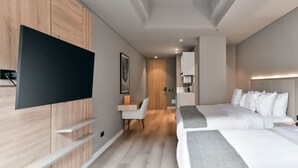 Ein modernes Hotelzimmer mit großem Flachbildfernseher, einem Schreibtisch mit Stuhl, zwei Betten und einem Kleiderschrank.