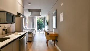Eine moderne Küche mit Mikrowelle, Spüle und Schränken, die in einen Schlafbereich mit Bett, Stuhl und Fenster führt.