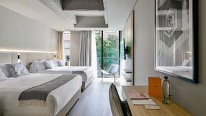 Ein modernes Hotelzimmer mit zwei Betten, einem Schreibtisch, einem Stuhl, einem großen Fenster und einem gerahmten Kunstwerk.