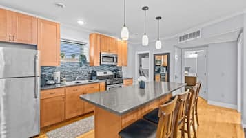 A modern kitchen with wooden cabinets, stainless steel appliances, a granite countertop island, and pendant lighting.