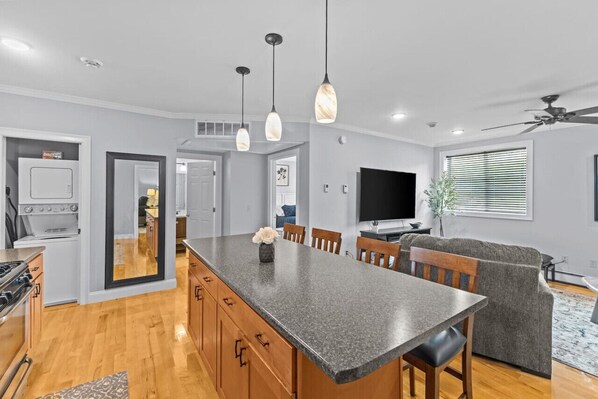 Una cocina moderna con encimeras de granito, armarios de madera, una isla central, iluminación colgante y un ventilador de techo.
