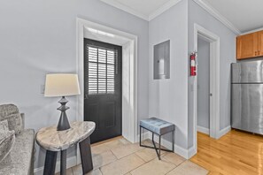 Una cocina moderna con un refrigerador de acero inoxidable, una mesa de mármol con una lámpara y una puerta oscura con persianas.
