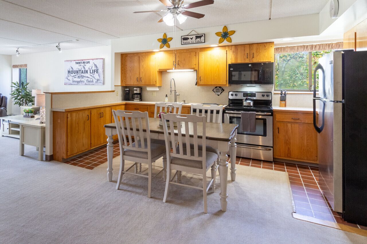 A kitchen with wooden cabinets, a dining table with chairs, a refrigerator, and a microwave.