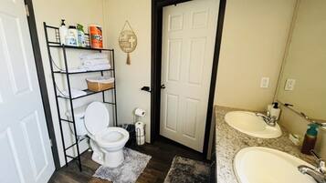 A bathroom with a toilet, a shelf with toiletries, a sink, and a door.