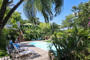 Un área de piscina con sillones de descanso, una terraza de madera y follaje tropical.