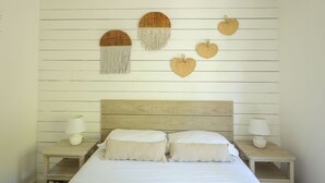 A bedroom with a wooden headboard, a bed with two pillows, and wall-mounted decorative items including a circular wooden piece with tassels and several heart-shaped items.