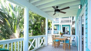 A covered porch with a ceiling fan, wooden chairs, and a table.