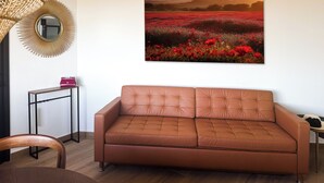 Un salón con un sofá de cuero marrón, un espejo redondo y un cuadro enmarcado de un paisaje.