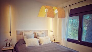 Un dormitorio con cama, mesitas de noche y ventana con vista a árboles.