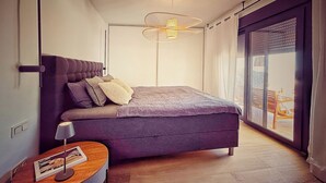 Un dormitorio moderno con una cama grande, una mesita de noche con lámpara y vistas a través de una puerta corrediza de vidrio.