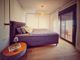 Un dormitorio moderno con una cama grande, una mesita de noche con lámpara y vistas a través de una puerta corrediza de vidrio.