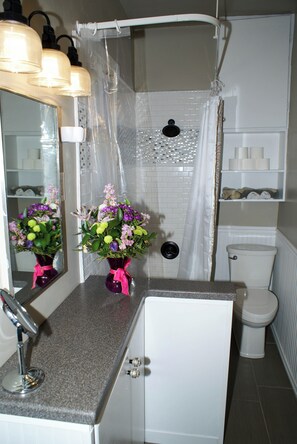 Un baño con ducha, inodoro y dos jarrones de flores en el mostrador.