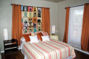 Un dormitorio con cama, dos mesitas de noche, un ventanal con cortinas y una pared decorada con un collage de imágenes de edificios.