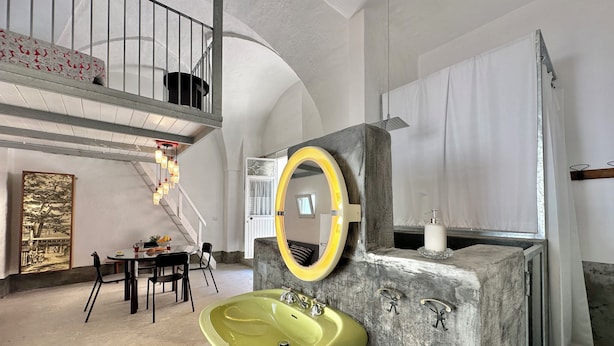Een moderne badkamer met een grote gele wastafel, een ronde spiegel en een accentmuur van steen.