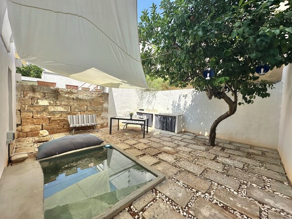 A patio with a glass table, a stone wall, a tree, and a white canopy. - Lu Parmientu - One Bedroom Apartment, Sleeps 2 (Parabita)