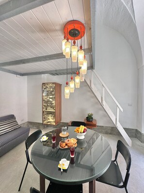 A dining area with a round glass table, black chairs, a fruit bowl, and a painting on the wall. - Lu Parmientu - One Bedroom Apartment, Sleeps 2 (Parabita)