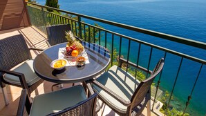 Ein Balkon mit einem für zwei Personen gedecktem Tisch, mit Blick auf ein Gewässer und ferne Berge.