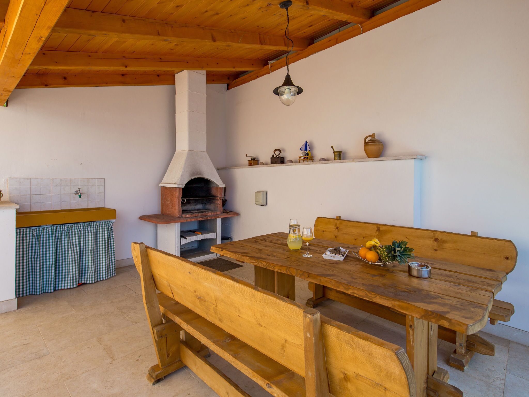 A rustic kitchen with a wood-burning stove, a wooden table with benches, and a tiled backsplash.